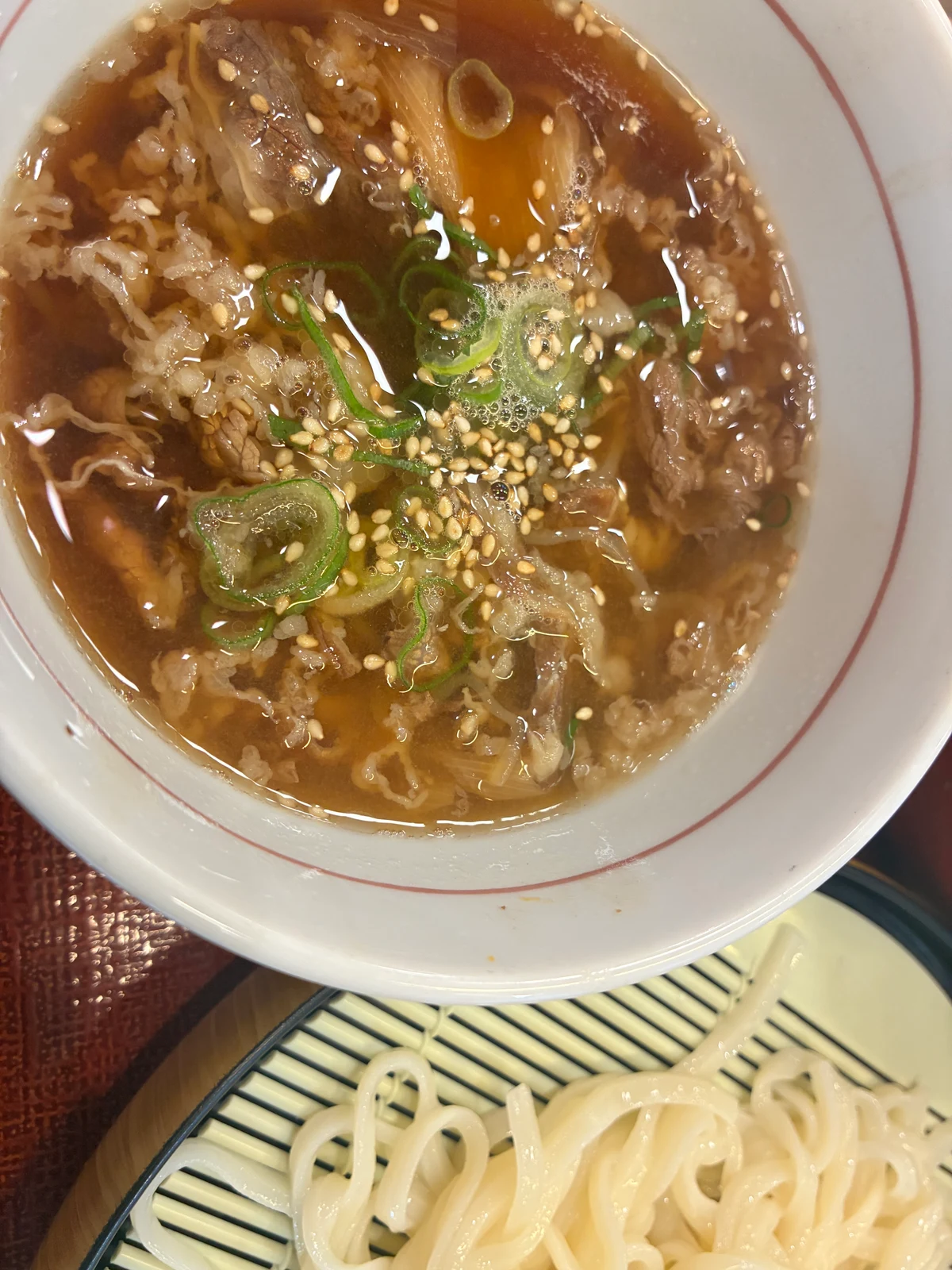 月見温たま牛肉つけうどんのつけ汁。薄切り牛肉、ねぎ、ごまが見える